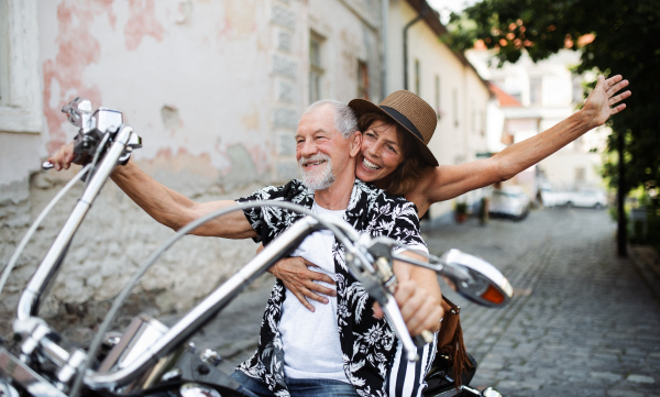 A front view of cheerful senior couple travellers with motorbike in town.