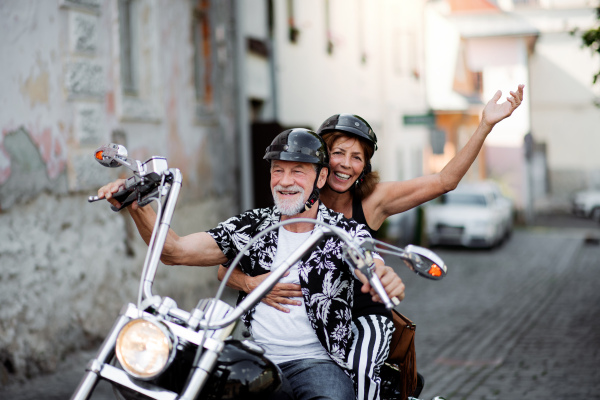 A front view of cheerful senior couple travellers with motorbike in town.