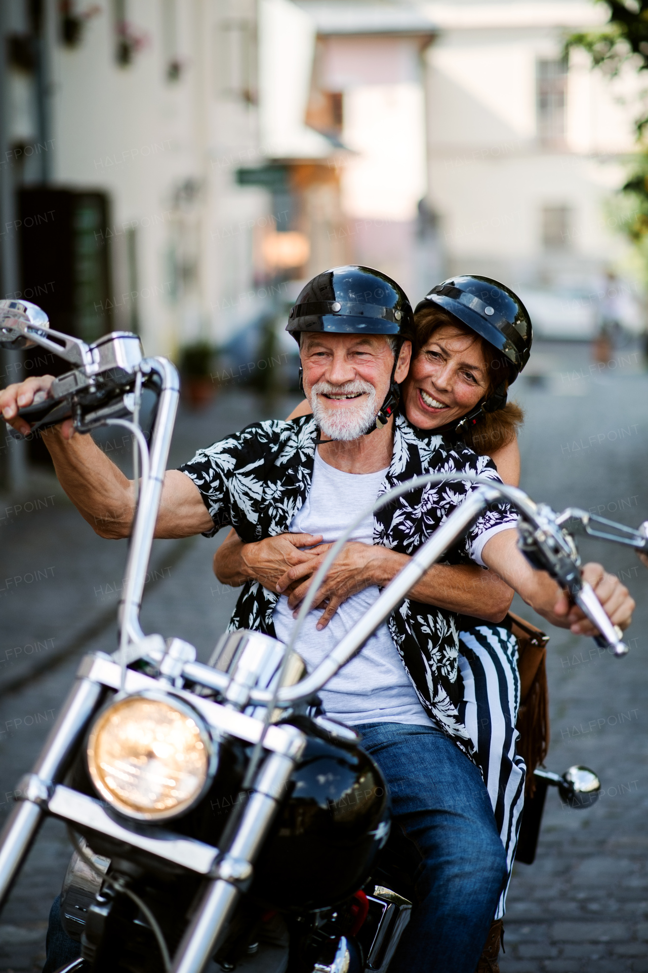 A front view of cheerful senior couple travellers with motorbike in town.