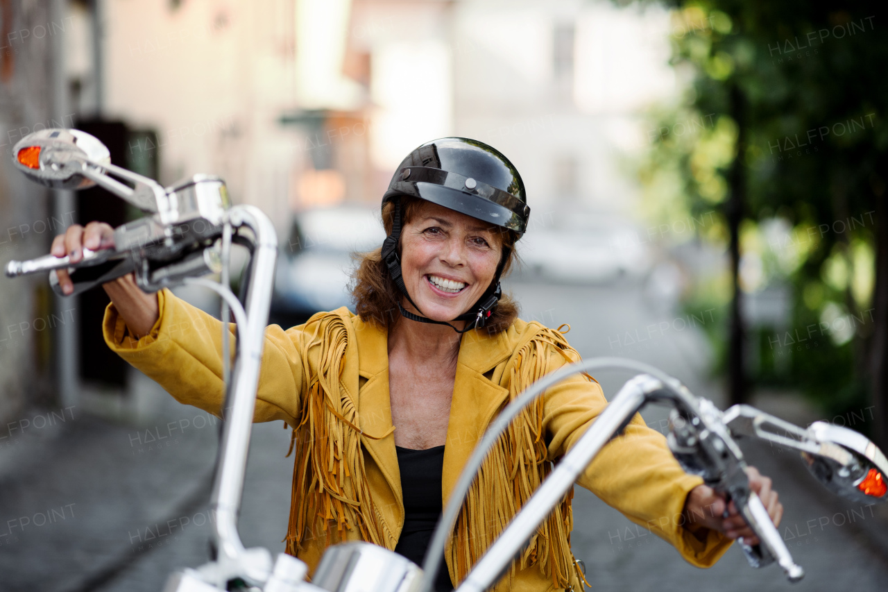 A cheerful senior woman traveller with motorbike in town, looking at camera.