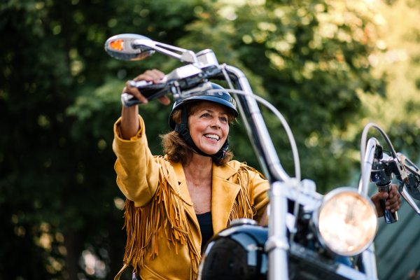 A cheerful senior woman traveller with motorbike in town.