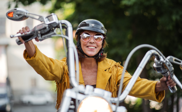 A cheerful senior woman traveller with motorbike in town.