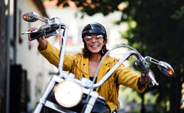 A cheerful senior woman traveller with motorbike in town.