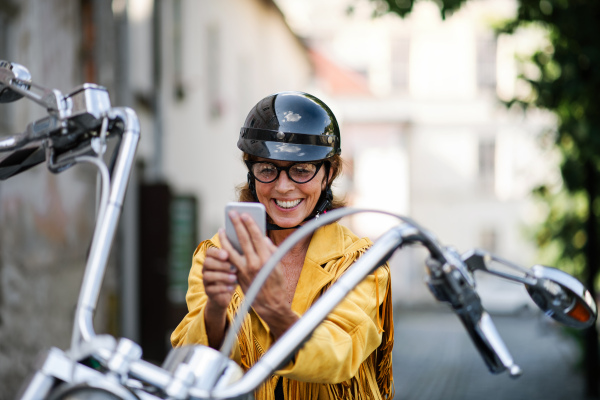 A cheerful senior woman traveller with motorbike in town, taking selfie.