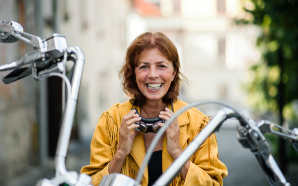 A cheerful senior woman traveller with motorbike in town.