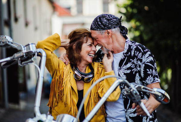 A front view of cheerful senior couple travellers in love with motorbike in town.