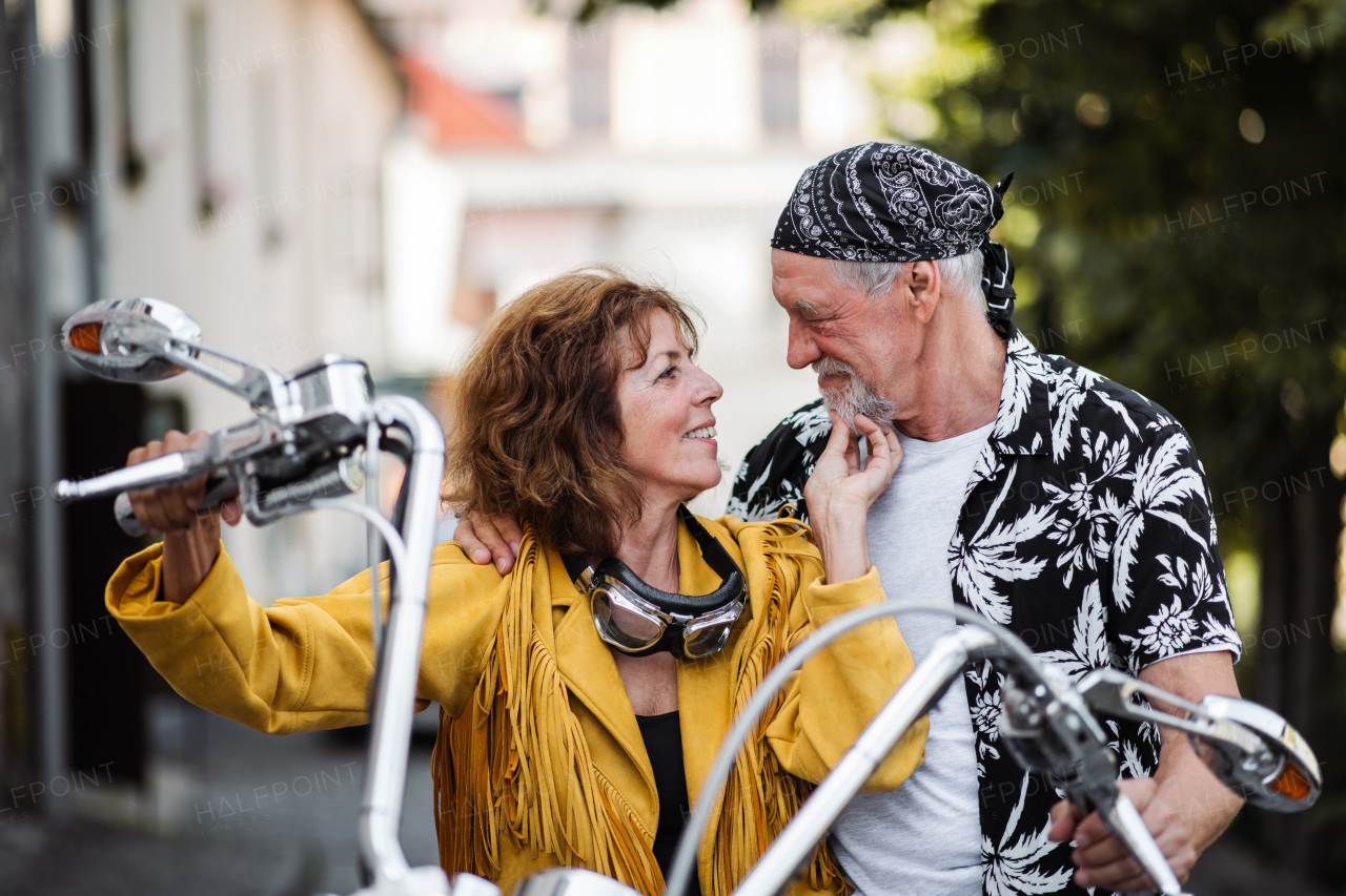 A front view of cheerful senior couple travellers in love with motorbike in town.