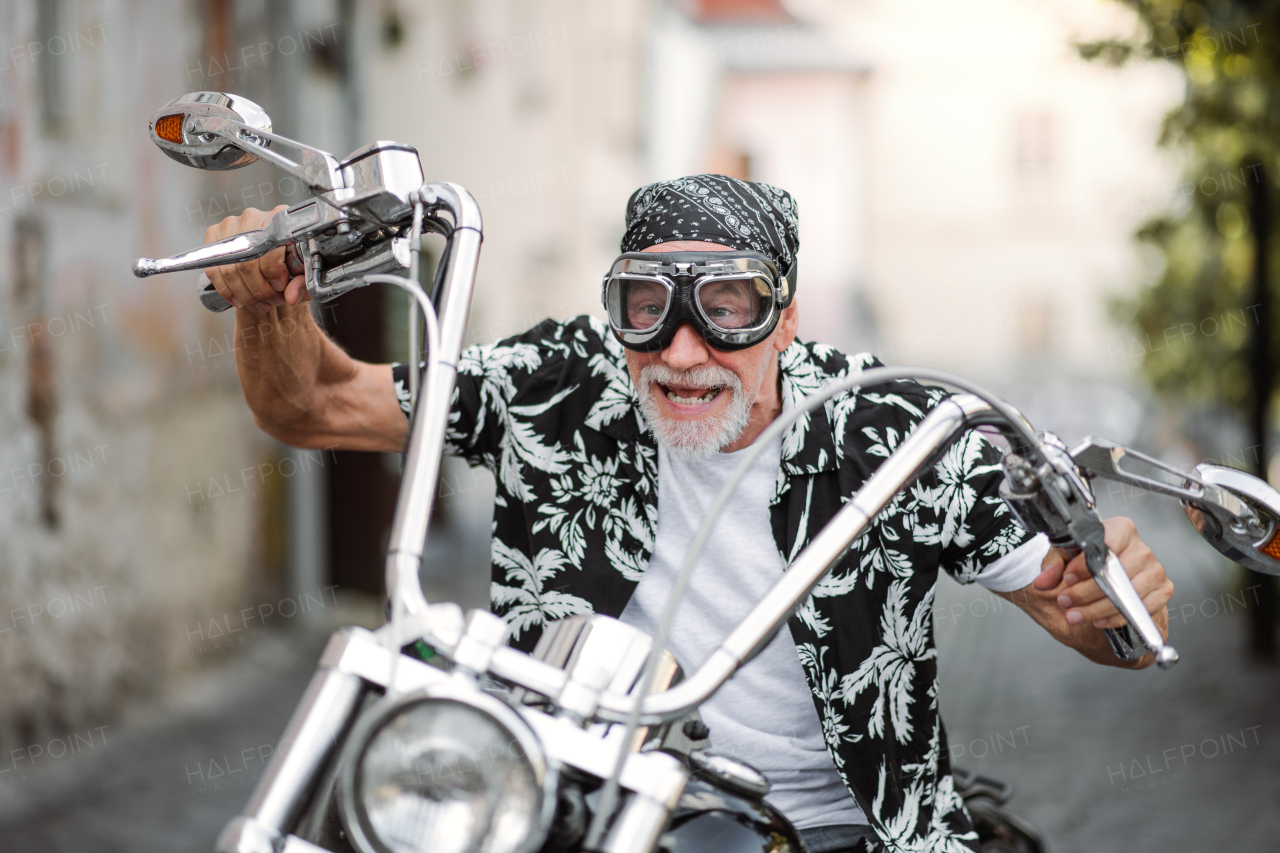 A front view of cheerful senior man traveller sitting on motorbike in town.