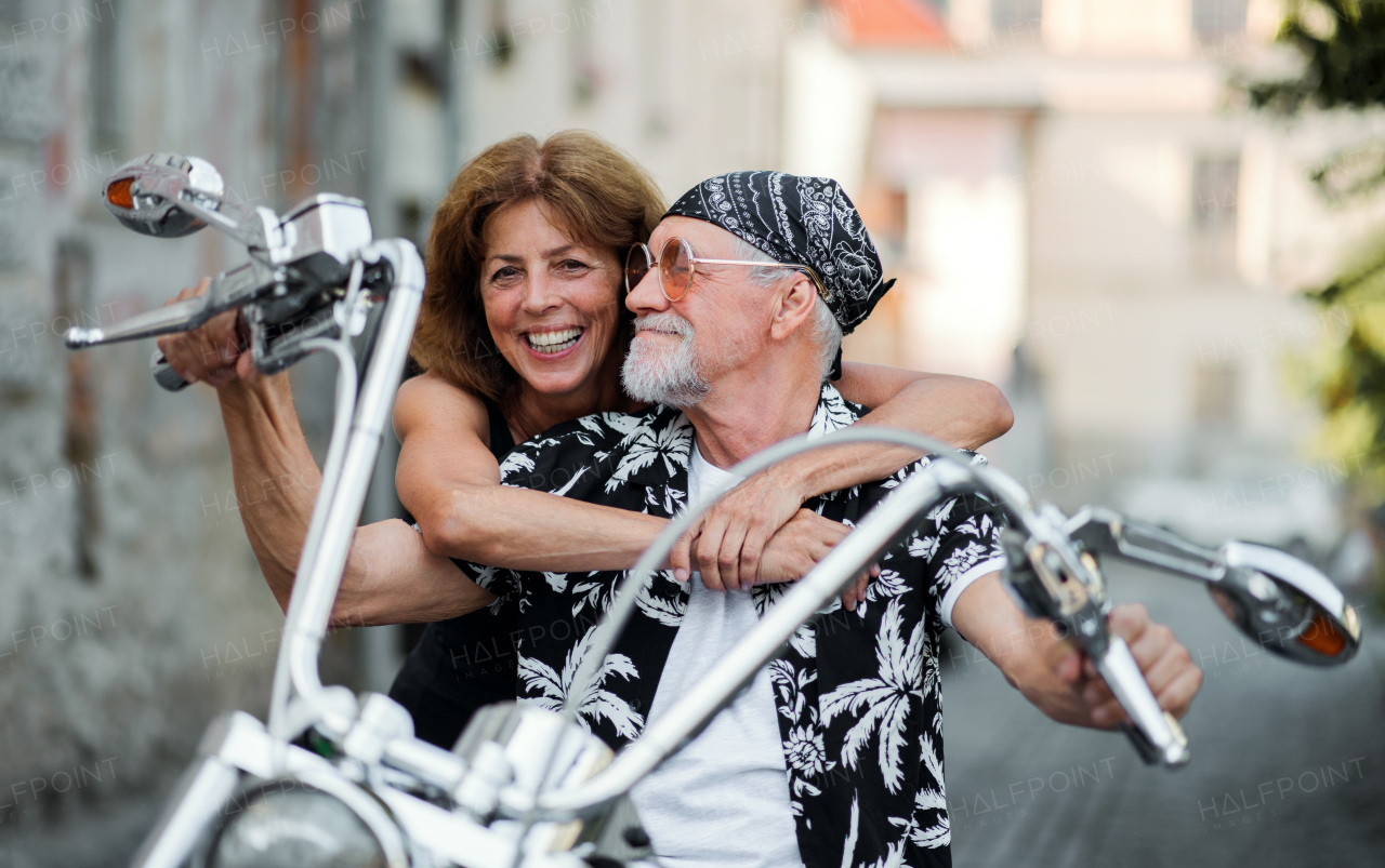 A front view of cheerful senior couple travellers with motorbike in town.