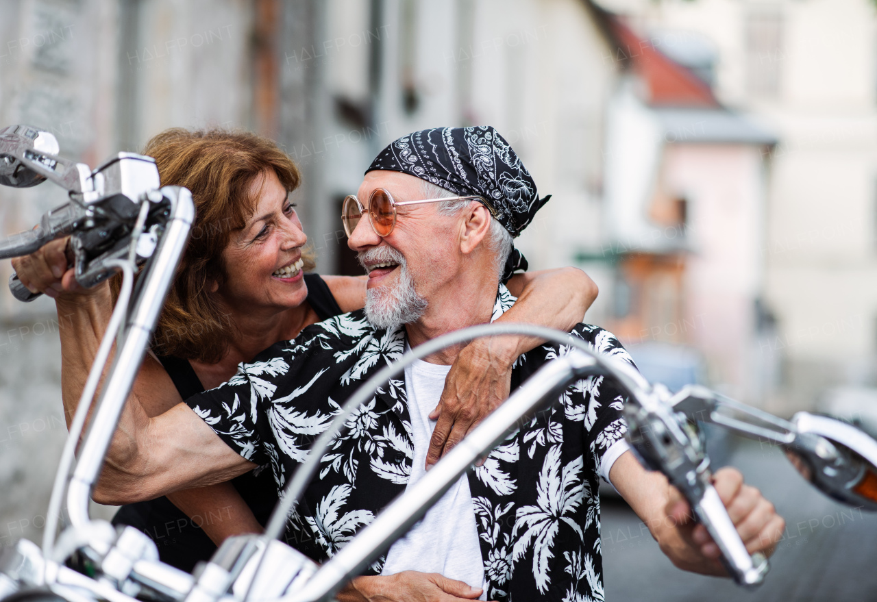 A front view of cheerful senior couple travellers with motorbike in town.