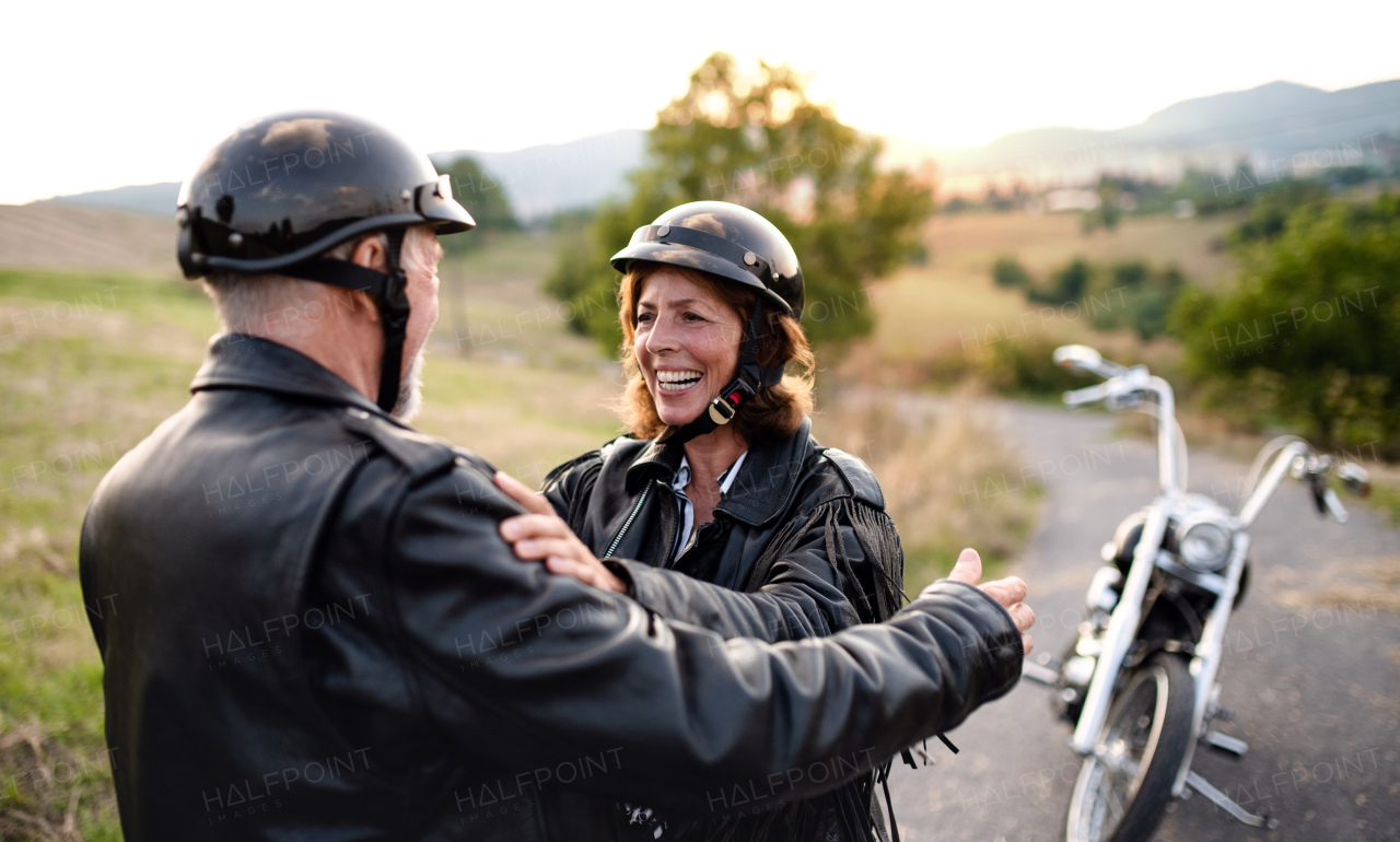 A cheerful senior couple travellers with motorbike in countryside, talking.