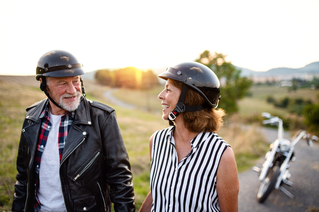 A portrait of cheerful senior couple travellers with motorbike in countryside, talking.