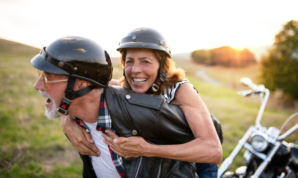 A cheerful senior couple travellers with motorbike in countryside, having fun.