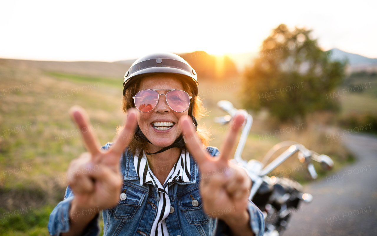 A cheerful senior woman traveller with motorbike in countryside, standing.