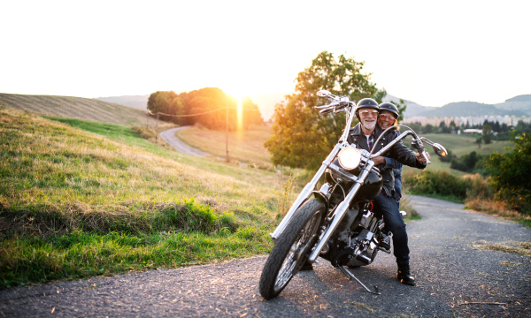 A cheerful senior couple travellers with motorbike in countryside. Copy space.