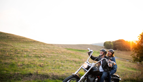 A cheerful senior couple travellers with motorbike in countryside. Copy space.