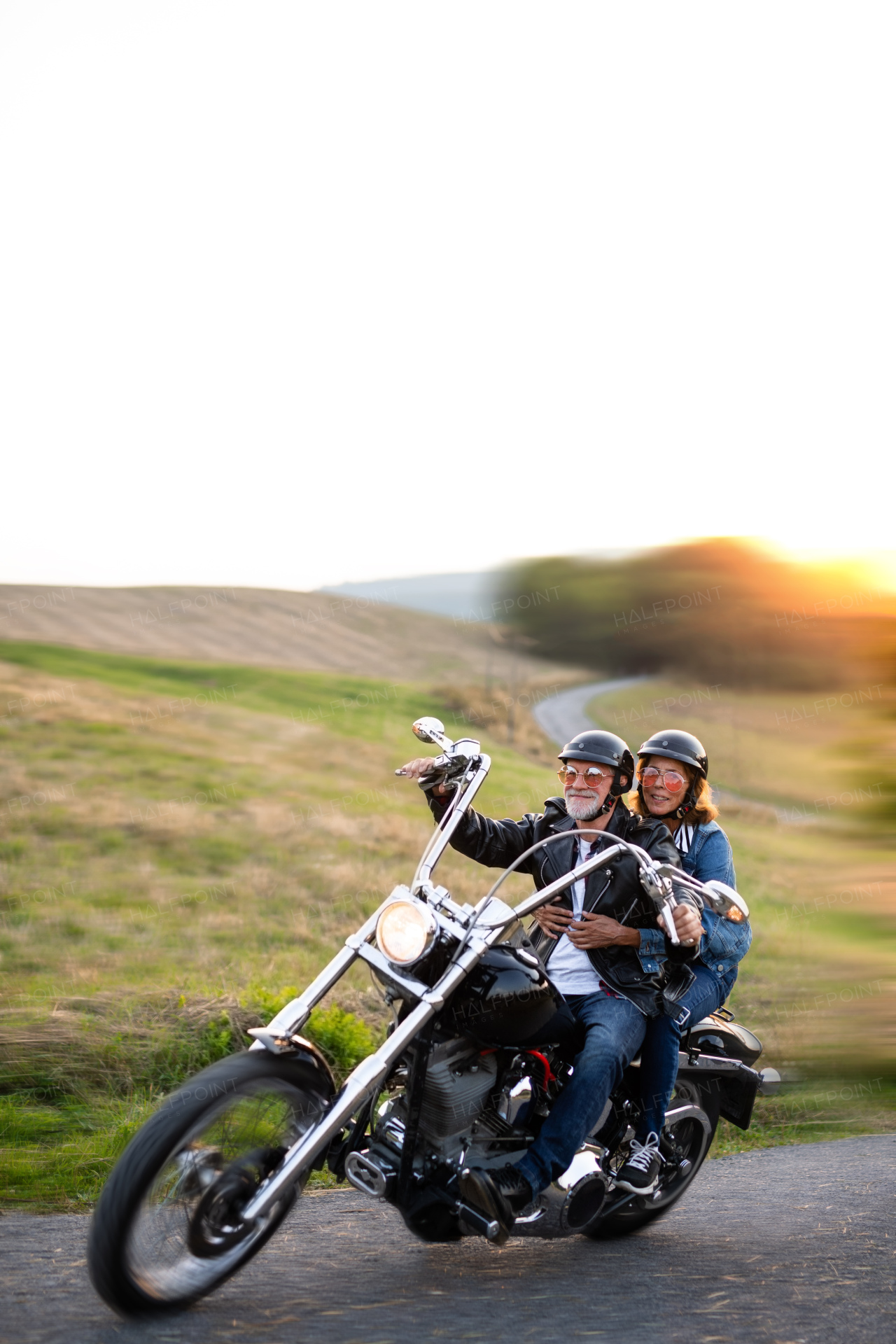 A cheerful senior couple travellers with motorbike in countryside. Copy space.