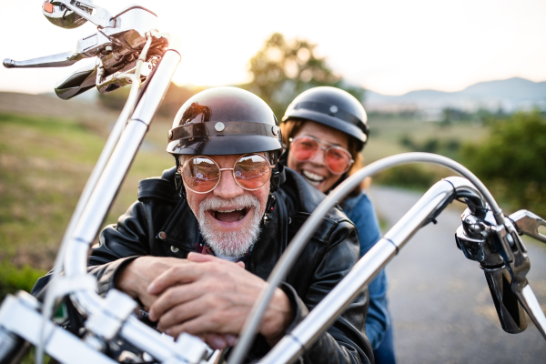 A cheerful senior couple travellers with motorbike in countryside. Copy space.