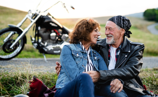 A front view portrait of senior couple travellers in love with motorbike in countryside.