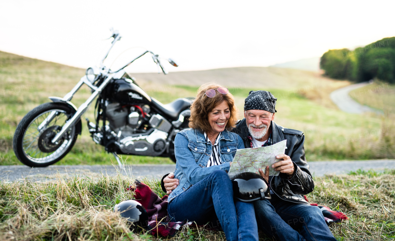 A cheerful senior couple travellers with map and motorbike in countryside.