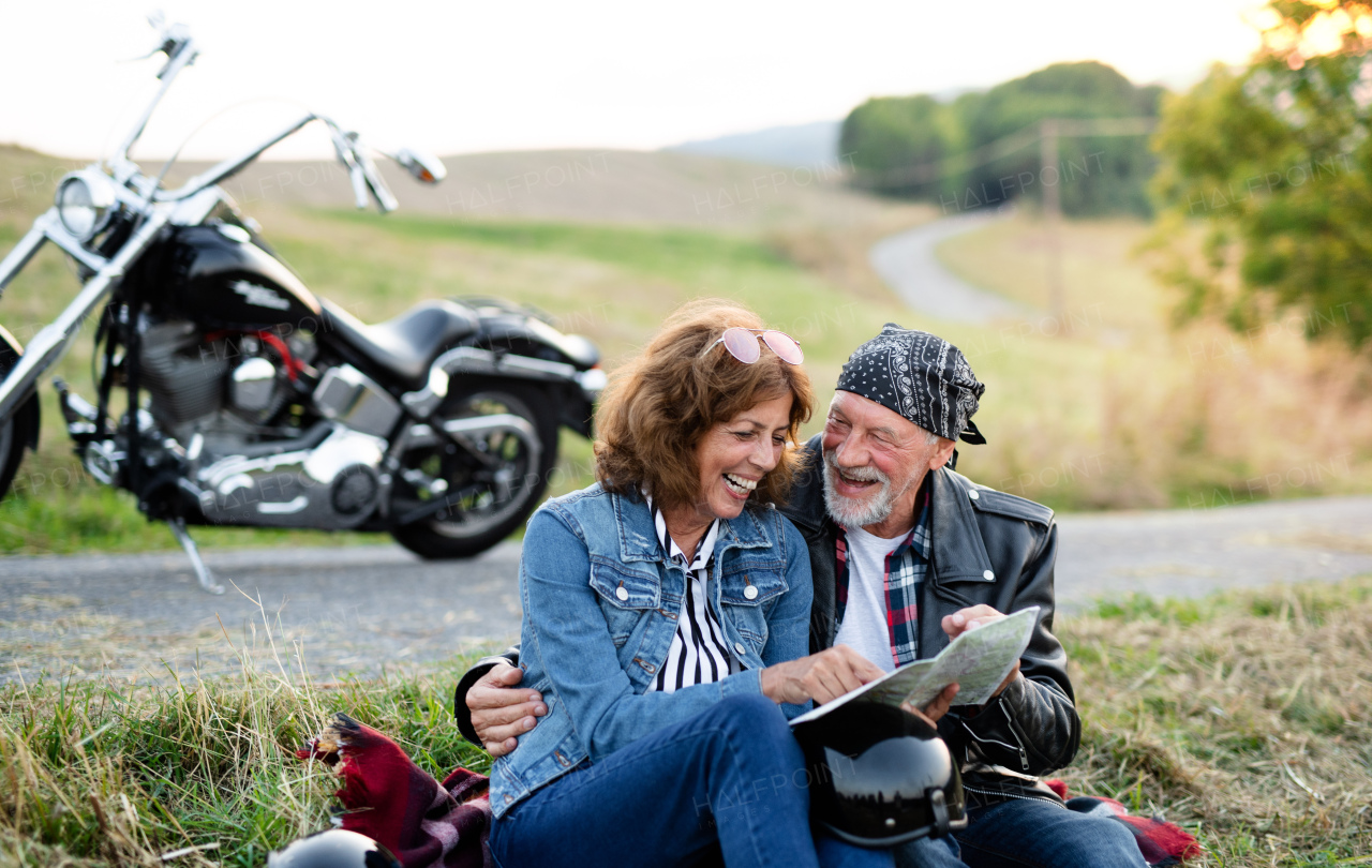 A cheerful senior couple travellers with map and motorbike in countryside.