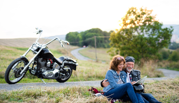 A cheerful senior couple travellers with map and motorbike in countryside.