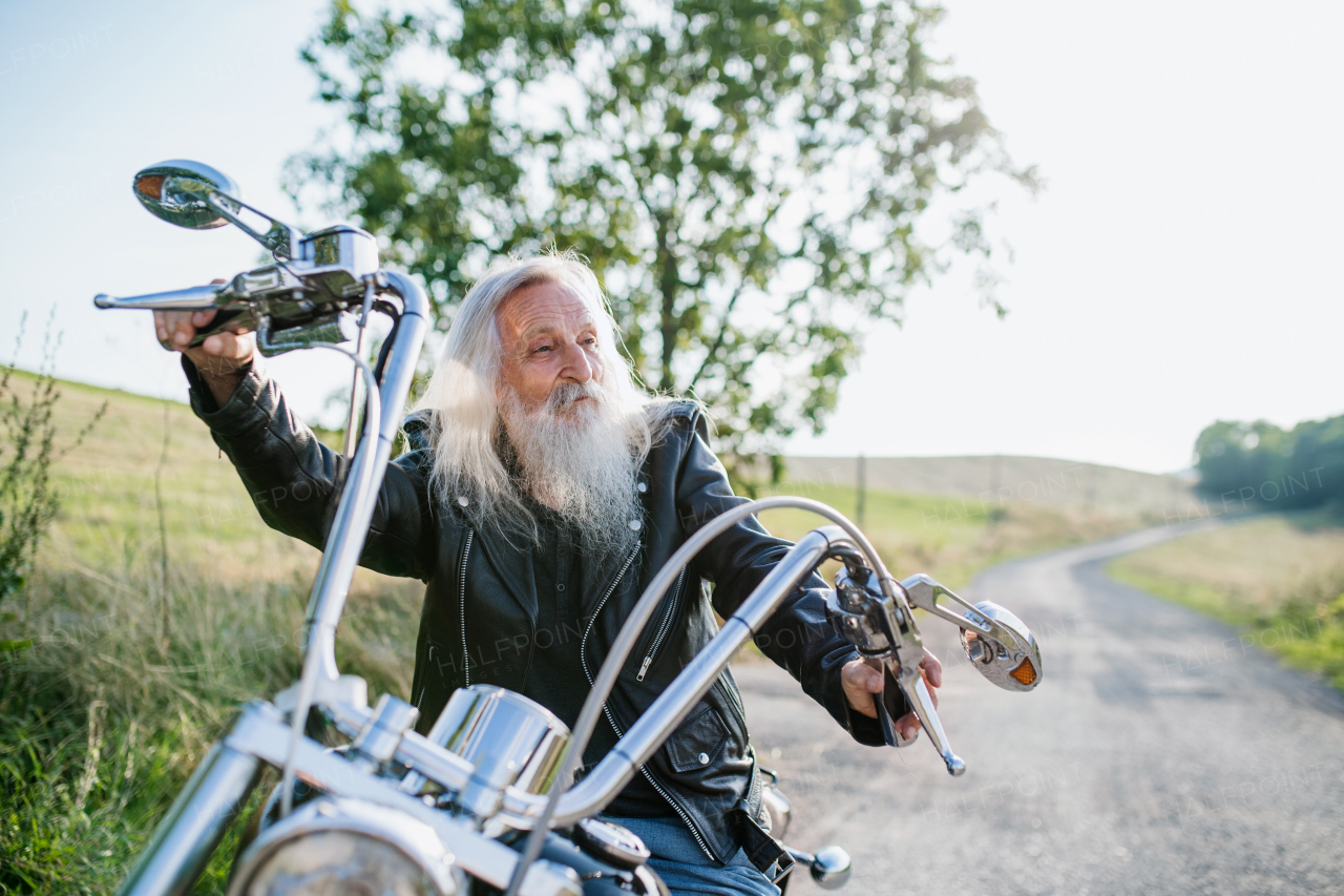 A senior man traveller with motorbike in countryside, resting.