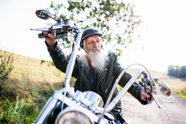 A senior man traveller with motorbike in countryside, resting.