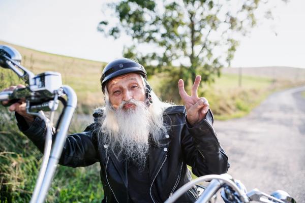 A senior man traveller with motorbike in countryside, resting.