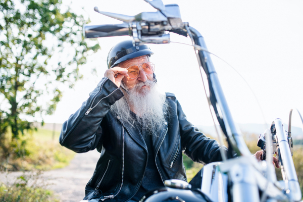 A senior man traveller with motorbike in countryside, resting.