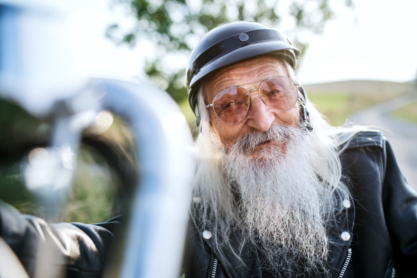 A senior man traveller with motorbike in countryside, resting.