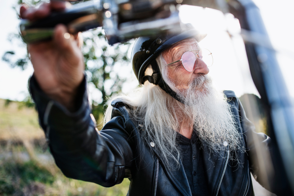 A senior man traveller with motorbike and sunglasses in countryside.