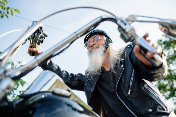 A senior man traveller with motorbike in countryside, resting.