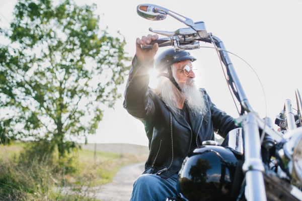 A senior man traveller with motorbike in countryside, resting.