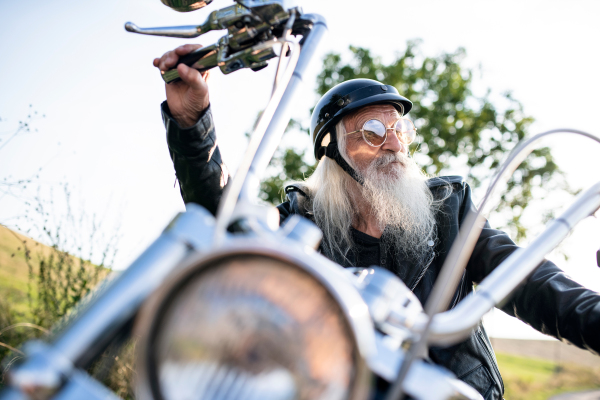 A senior man traveller with motorbike and sunglasses in countryside.