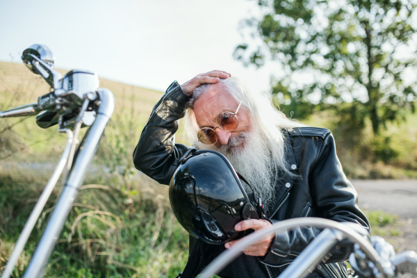 A senior man traveller with motorbike in countryside, resting.