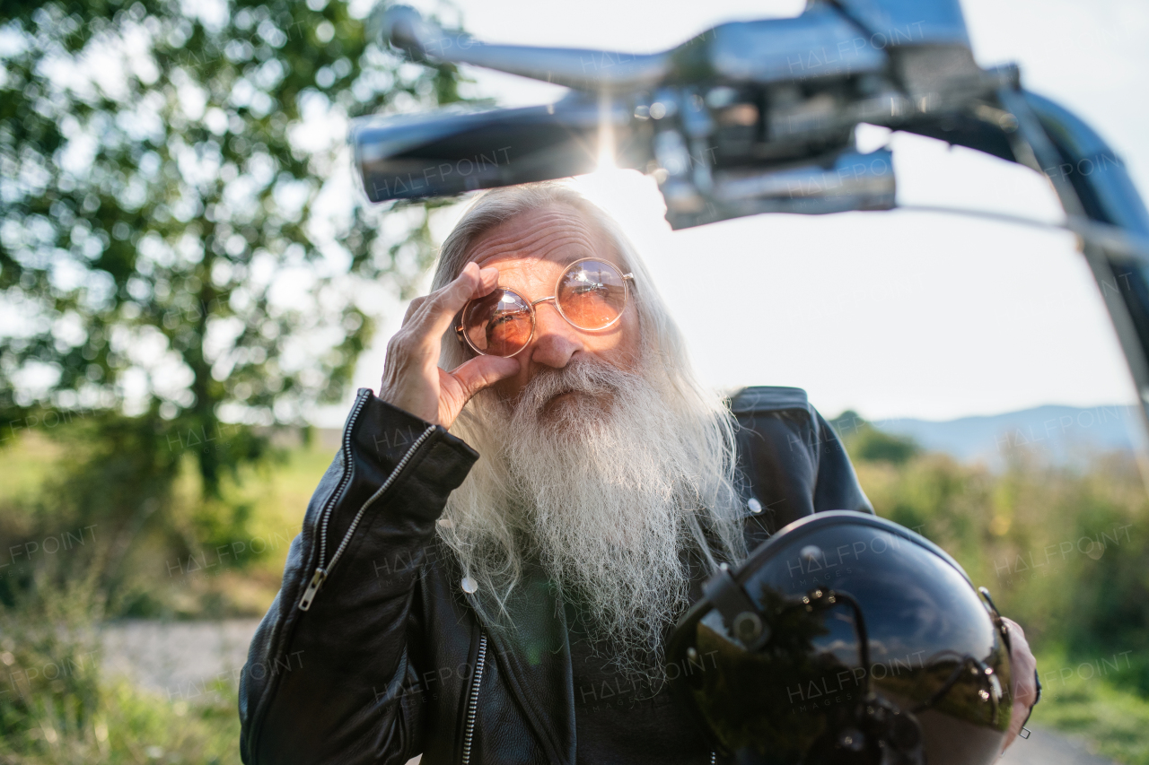 A senior man traveller with motorbike and sunglasses in countryside.