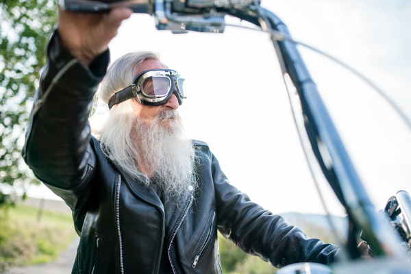 A senior man traveller with motorbike and goggles on road in countryside. Copy space.