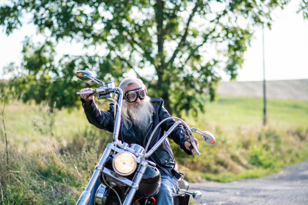 A senior man traveller with motorbike and goggles on road in countryside. Copy space.