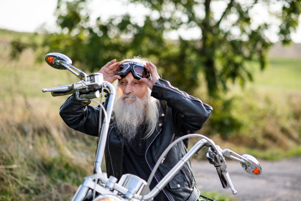 A senior man traveller with motorbike on road in countryside. Copy space.