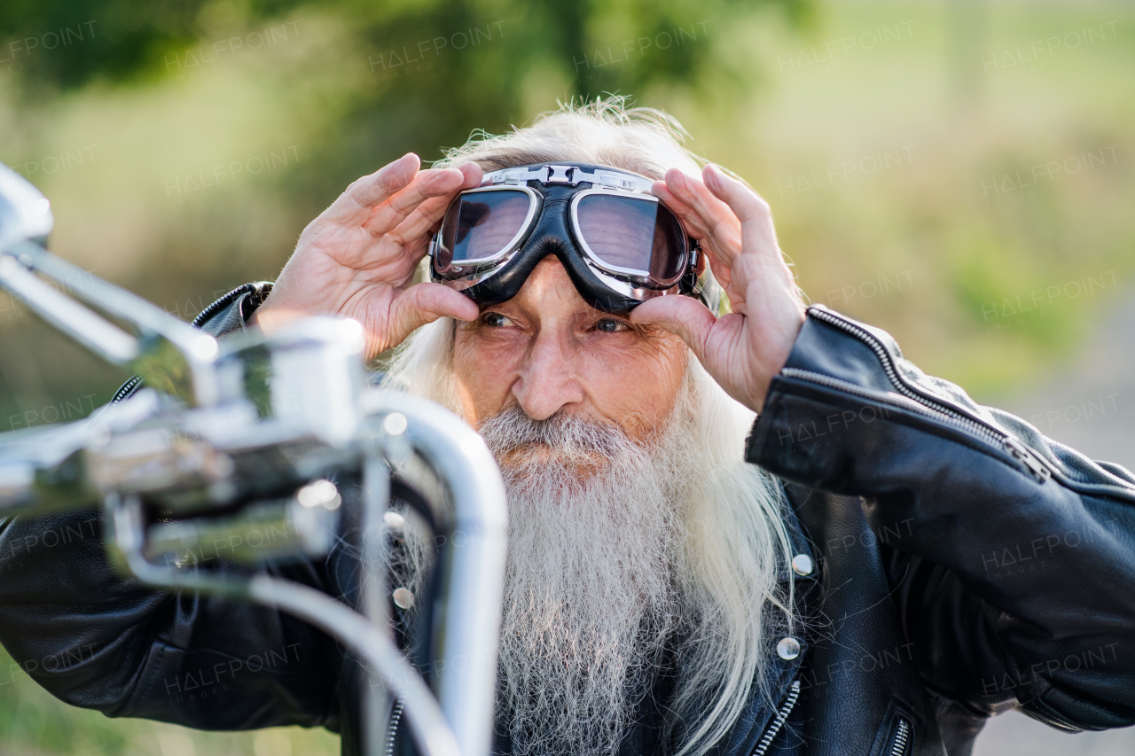 A senior man traveller with motorbike and goggles on road in countryside.