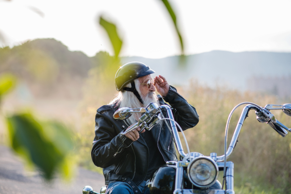 A senior man traveller with motorbike and sunglasses in countryside.