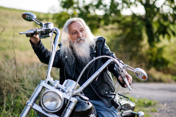 A senior man traveller with motorbike in countryside, resting.