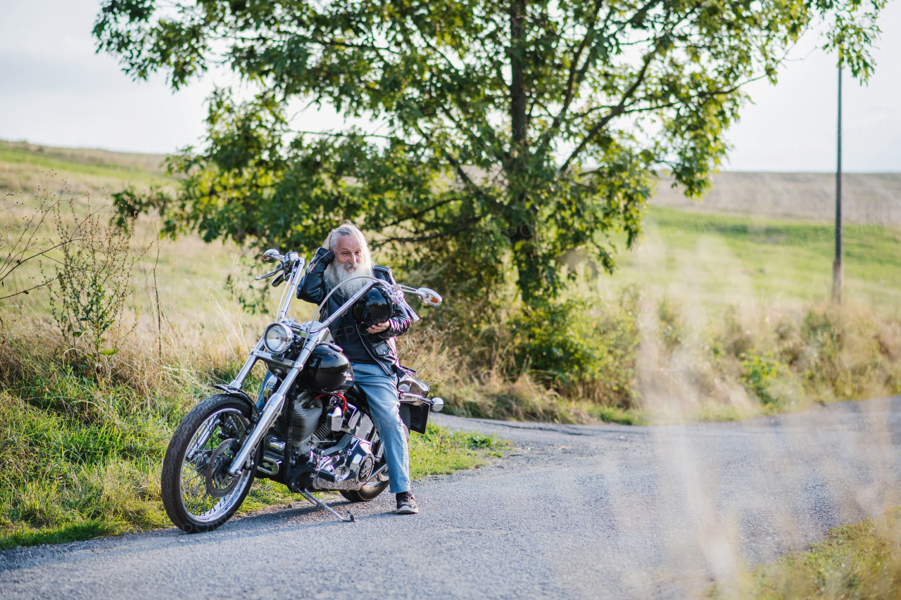 A senior man traveller with motorbike on road in countryside. Copy space.