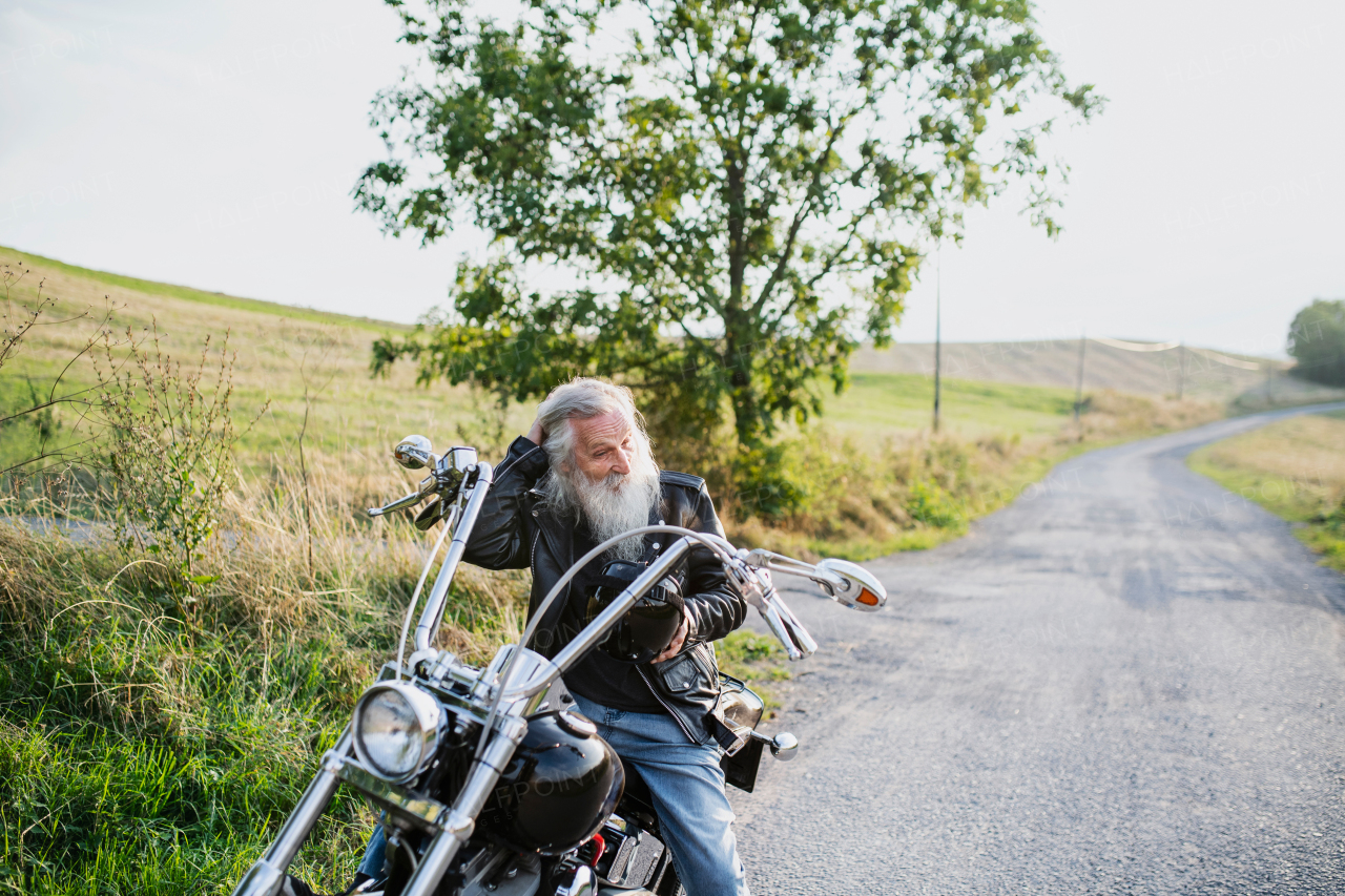 A senior man traveller with motorbike on road in countryside. Copy space.