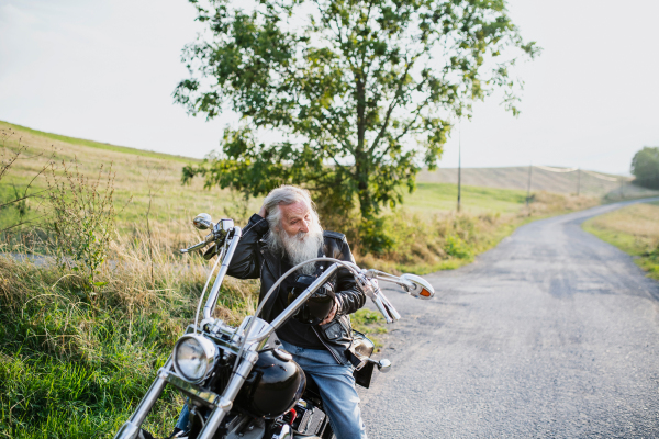 A senior man traveller with motorbike on road in countryside. Copy space.