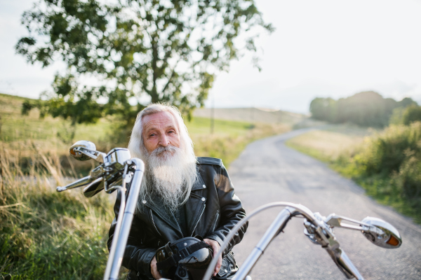 A senior man traveller with motorbike in countryside, resting.