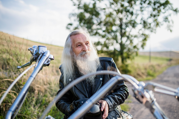 A senior man traveller with motorbike in countryside, resting.