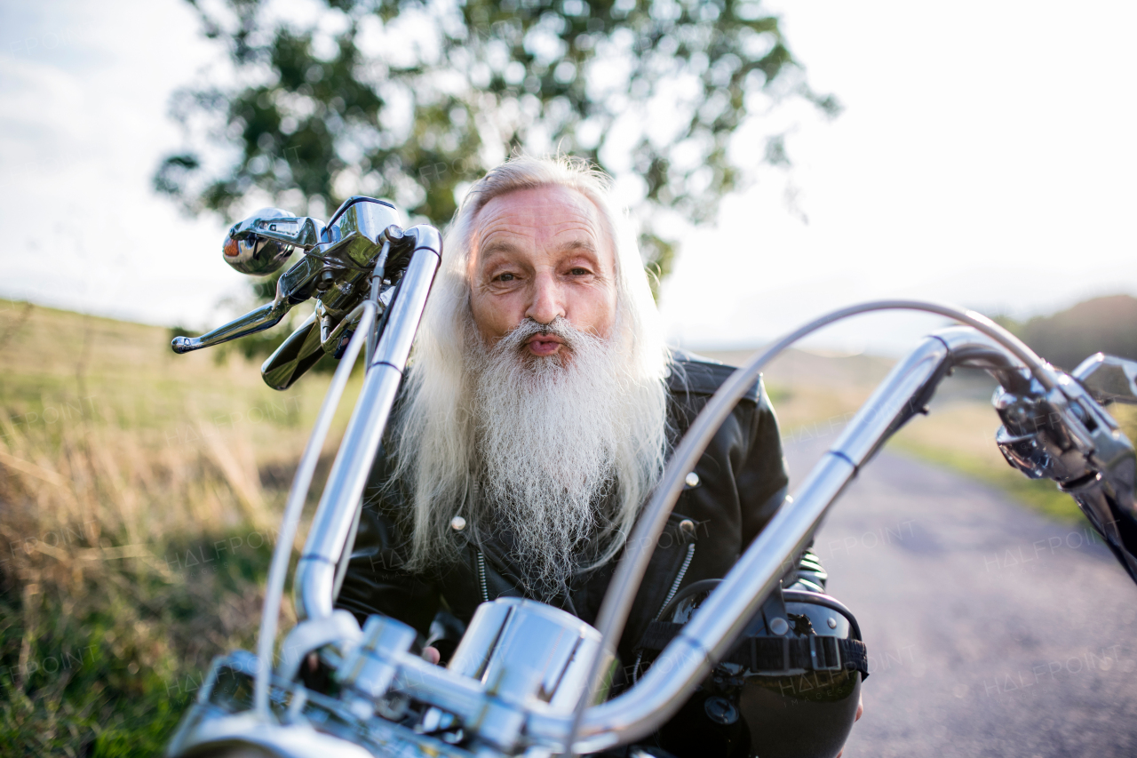 Front view of senior man traveller with motorbike in countryside, having fun.