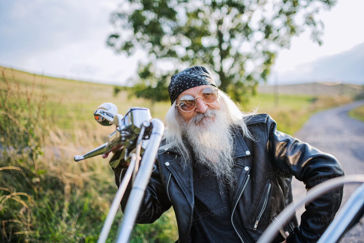 A senior man traveller with motorbike and sunglasses in countryside.